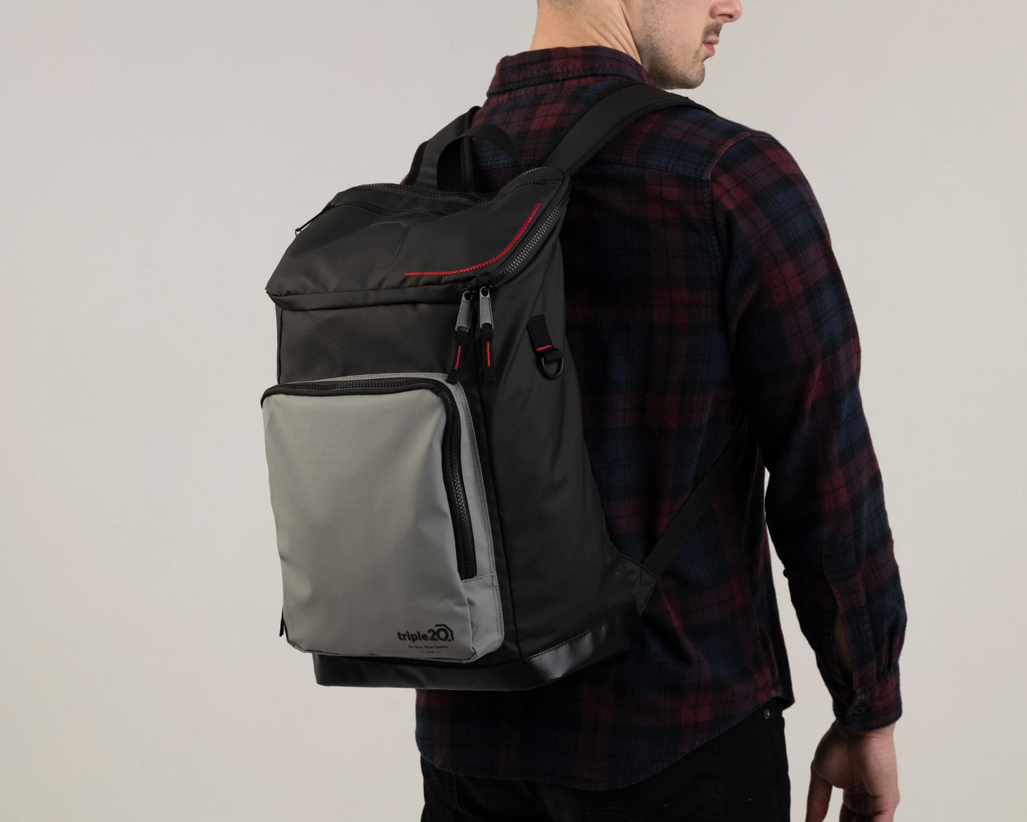 Foto eines männlichen Models, der einen triple20 Dartschuh auf dem Rücken trägt. Der Rucksack ist sehr hochwertig und verfügt über zahlreiche interessante Details sowie ein hohes Maß an Funktionalität. Das Foto zeigt, dass der schwarz-graue Rucksack mit den roten Details nicht nur praktisch sondern gleichzeitig sehr stylisch ist.